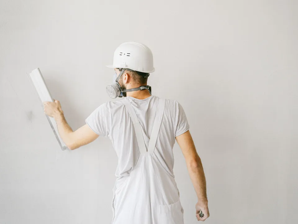 A plasterer in safety gear skimming a white wall