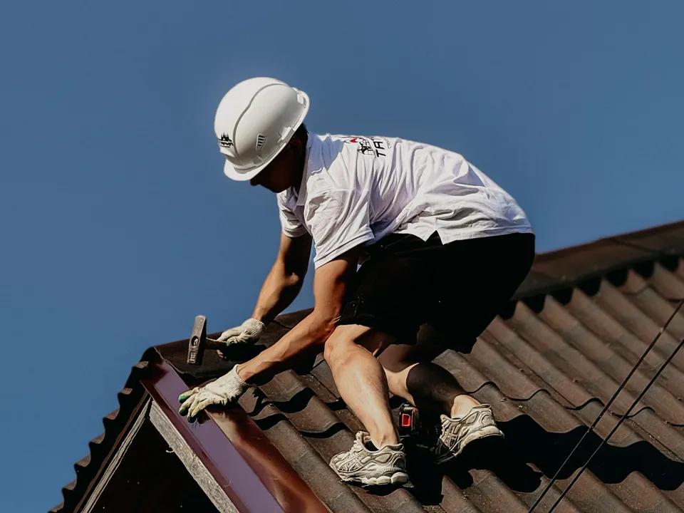 A roofer in a safety helmet working on the tiled roof of a brick house